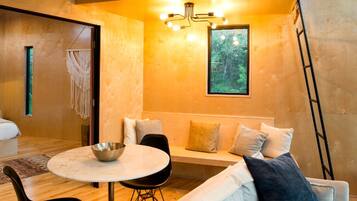 A cozy room with a round table, black chairs, a sofa with cushions, a macrame wall hanging, and a framed picture.