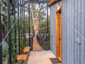 Un chemin en bois mène à un bâtiment doté d’une structure métallique, avec un arbre en arrière-plan.