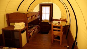 A tent with bunk beds, a small table, and a chair. - Rustic Conestoga Wagon Stay with Lodge Amenities near Boulder Creek, Montana (Hall)