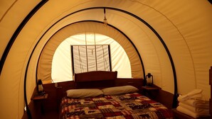 A tent with a bed, a window, a lantern, and a folded towel. - Rustic Conestoga Wagon Stay with Lodge Amenities near Boulder Creek, Montana (Hall)