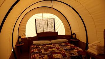 Una tienda de campaña con una cama, una ventana, un farol y una toalla doblada.