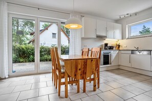 A modern kitchen with a dining table and chairs, a built-in oven, and a large window. - Apartment 'Haus 44 EG' with Lake View, Private Terrace and Wi-Fi (Röbel)