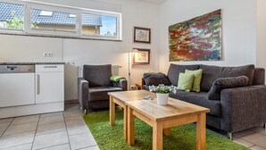 Um espaço de estar moderno com cozinha, sofá cinza, mesa de centro de madeira e tapete verde.