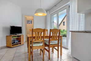 A dining area with a table and chairs, a television on a stand, and a sliding glass door leading outside. - Apartment 'Haus 44 EG' with Lake View, Private Terrace and Wi-Fi (Röbel)
