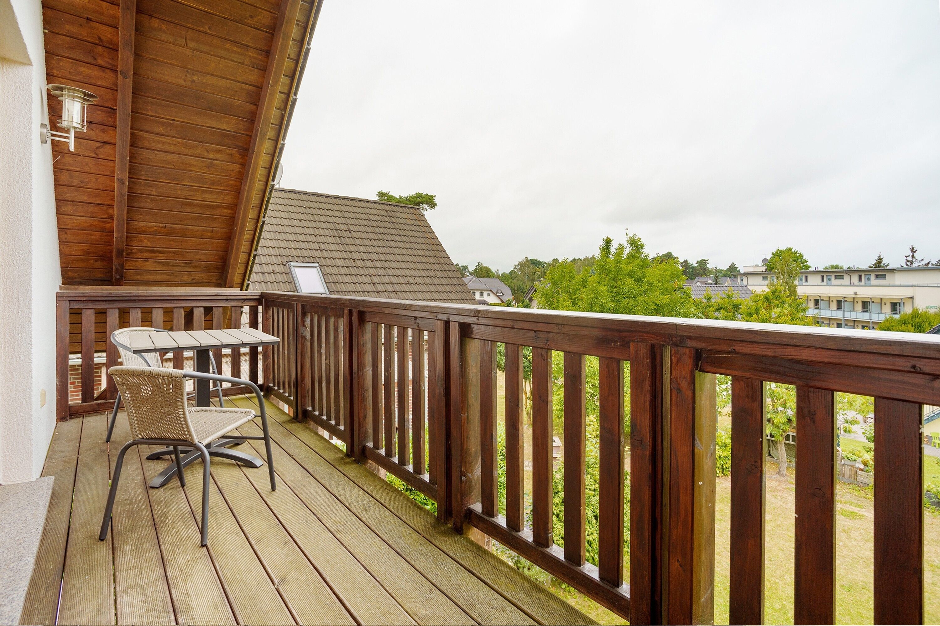 Une terrasse en bois avec une table et des chaises, une rambarde et une vue sur les environs.