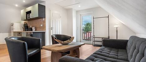 A modern living space with a sofa, a dining table, a kitchen area, and a balcony with a view.