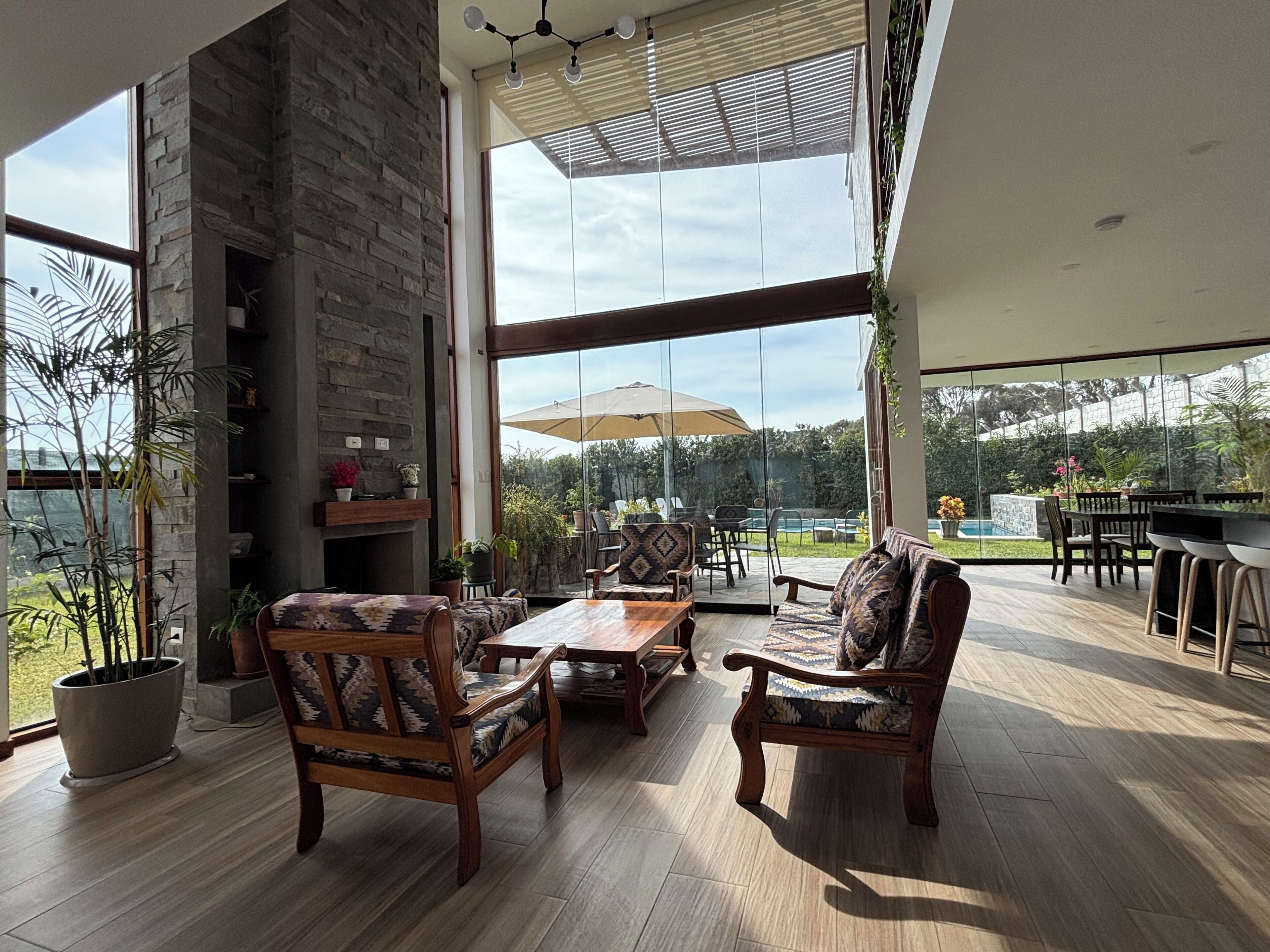 A spacious patio with wooden furniture, a stone fireplace, and large windows offering a view of the outdoors.