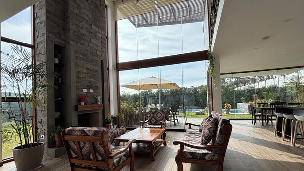 A spacious patio with wooden furniture, a stone fireplace, and large windows offering a view of the outdoors.