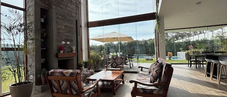 A spacious patio with wooden furniture, a stone fireplace, and large windows offering a view of the outdoors.