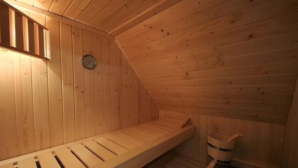 Un cuarto de sauna con paredes de madera, un banco, un reloj y un pequeño calentador.