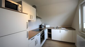 Una cocina moderna con armarios blancos, horno empotrado, microondas y cafetera.
