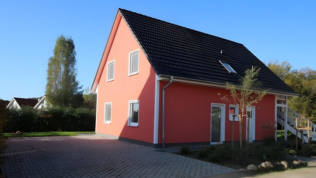 Een rode woning met een zwart dak, witte ramen en een kleine boom ervoor.