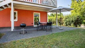 Een rood gebouw met een balkon, een barbecue en buiten zitplaatsen.