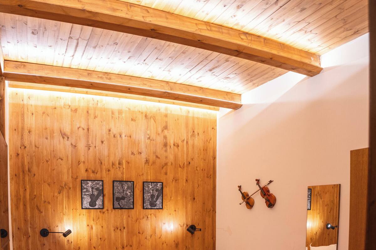 A wooden-paneled bedroom with a bed, bedside tables, a mirror, and wall-mounted violin art.