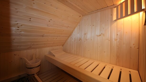 Una sauna con paredes y bancos de madera, un calentador para bancos y un pequeño armario de madera.