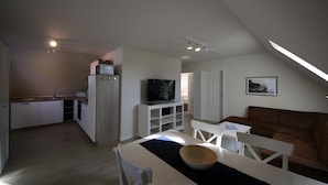 Una cocina moderna con armarios blancos, una zona de comedor con mesa y sillas, un televisor y un sofá de cuero marrón.