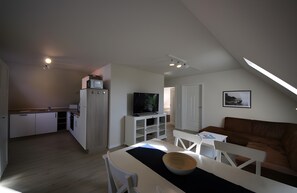 Eine moderne Küche mit weißen Schränken, einem Essbereich mit Tisch und Stühlen, einem Fernseher und einem braunen Ledersofa.