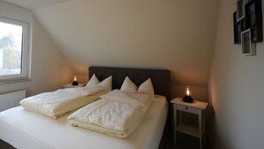 Un dormitorio con una cama, dos mesitas de noche, una ventana y una estantería de pared.