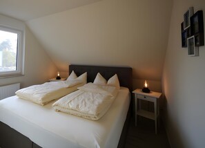 Ein Schlafzimmer mit einem Bett, zwei Nachttischen, einem Fenster und einem an der Wand befestigten Regal.