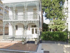 A two-story building with a balcony, potted plants, and a brick pathway. - Old World 2bd | Walk to Conventions & Street Car (New Orleans)