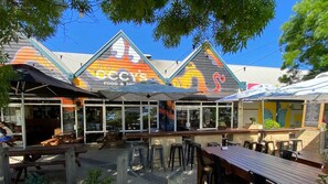 Un restaurante con fachada colorida, mesas al aire libre y un cartel de menú visible.