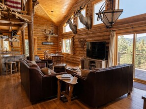 Interior de una cabaña de madera con chimenea, muebles de cuero, cabezas de animales montadas en la pared y un televisor grande.