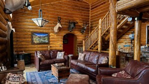 A log cabin interior with leather furniture, a dining area, and a staircase. - Fabulous 5-bedroom cabin in Westcliffe perfect for your getaway (Westcliffe)
