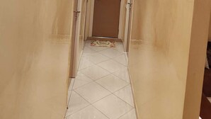Un corridoio con pavimento piastrellato, una porta in fondo e illuminazione a incasso nel soffitto.