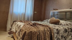 Una camera da letto con un letto, una finestra con tende, un termosifone a muro e un elemento decorativo.