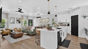 A modern kitchen with a central island, a dining area with a sofa and chairs, and a living room with a ceiling fan.