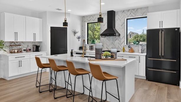 A modern kitchen with white cabinetry, a central island with bar stools, a black refrigerator, and a large window offering a view.