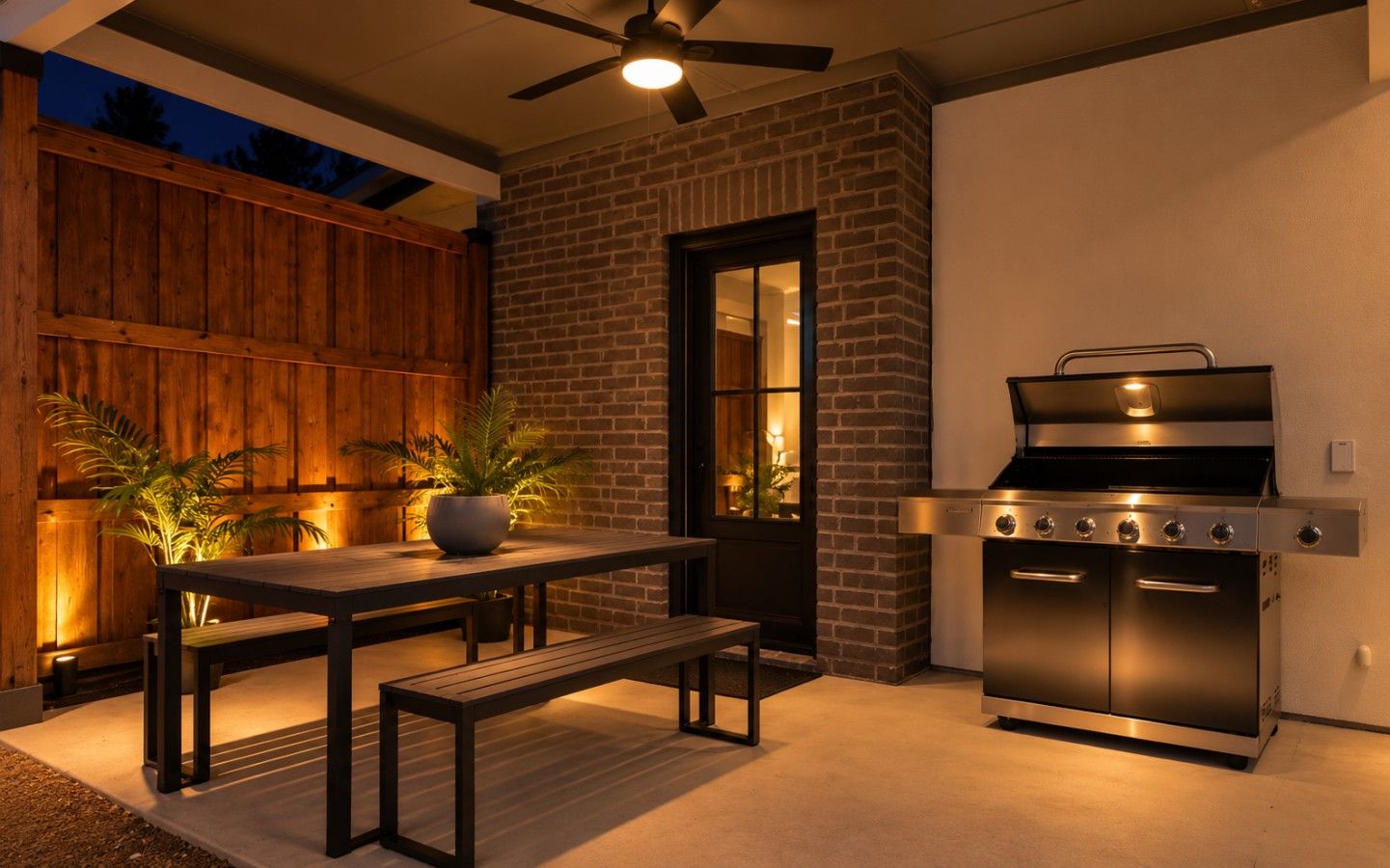An outdoor patio with a brick wall, a wooden fence, a table with benches, and a built-in grill.
