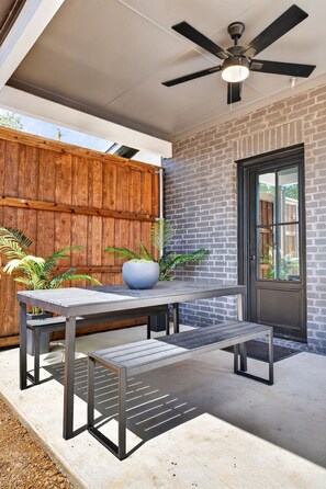 An outdoor patio with a table and benches, a ceiling fan, and a brick wall. - Luxury Townhome D. Walk to AT&T Stadium. Rooftop Terrace + Game Room. Sleeps 10. (Arlington)