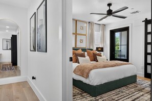 A modern bedroom with a large bed, a ceiling fan, and a view of the outdoors. - Luxury Townhome D. Walk to AT&T Stadium. Rooftop Terrace + Game Room. Sleeps 10. (Arlington)