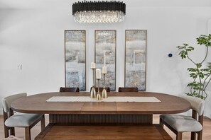 A dining room with a round table, three tall abstract paintings, a chandelier, and a potted plant. - Luxury Townhome D. Walk to AT&T Stadium. Rooftop Terrace + Game Room. Sleeps 10. (Arlington)