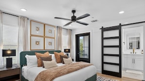 A bedroom with a bed, bedside tables, a ceiling fan, a door leading to a balcony, and a bathroom with a mirror and sink. - Luxury Townhome D. Walk to AT&T Stadium and Globe Life Fields. Rooftop + Game Rm (Arlington)