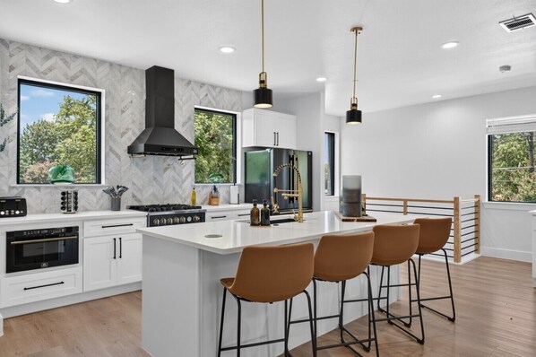 A modern kitchen with white cabinetry, a central island with bar stools, a black range hood, and pendant lighting.