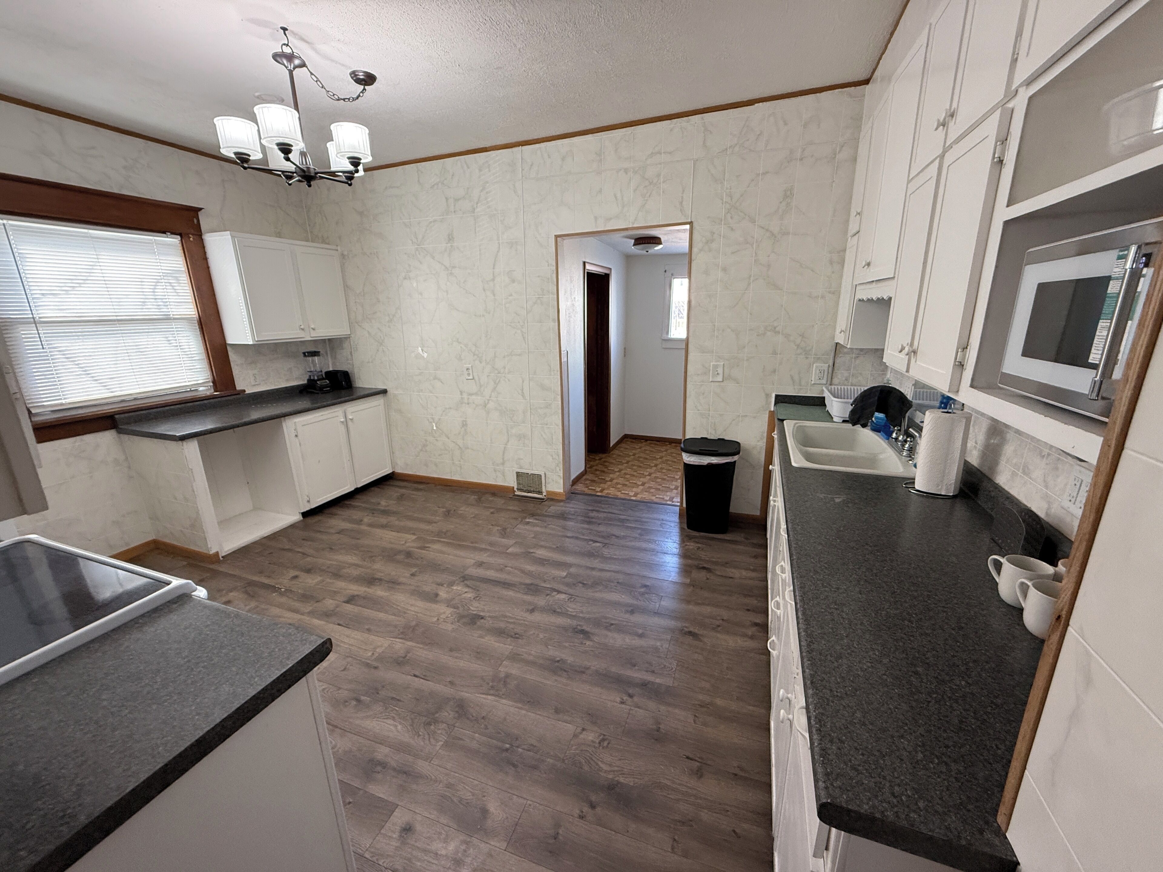 A kitchen with marble walls, a wooden floor, a built-in microwave, and a ceiling light fixture.