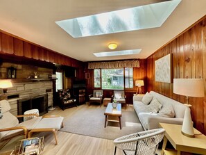 A cozy living room with a fireplace, wooden walls, a sofa, and a skylight. - BeachyBu 3-bedroom Michiana cottage 2 blocks to Lake (New Buffalo)