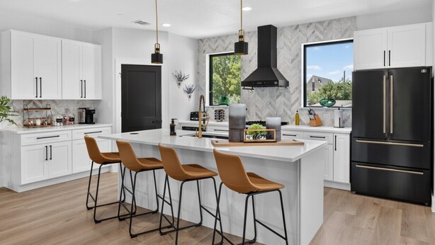 A modern kitchen with white cabinetry, a central island with bar stools, a black refrigerator, and a large window offering a view. - Luxury Townhome A. Walk to AT&T Stadium. Rooftop Terrace + Game Room. Sleeps 10. (Arlington)