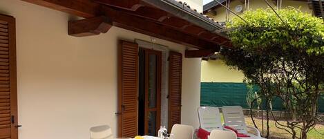 A patio with a table set for two, surrounded by chairs, and a small garden area with a tree and a fence.