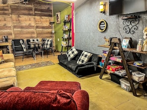 A cozy living room with a sofa, a red chair, a coffee table, a bookshelf, and a TV mounted on the wall.