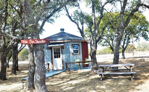 A rustic cabin labeled 'The Six Shooter' with a wooden bench and picnic table nearby, surrounded by trees.