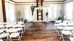 A room with wooden beams, white walls, and a wooden floor. There are white chairs arranged in rows.