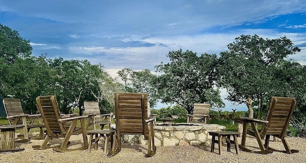 Outdoor seating with a stone fire pit, surrounded by trees and a clear sky.