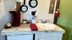 A kitchen with a sink, a red kettle, and a small cabinet.