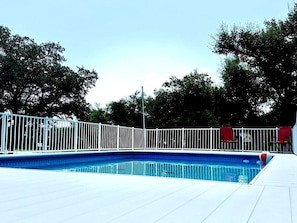 A swimming pool with a white fence, surrounded by trees.