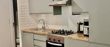 A modern kitchen with a built-in oven, a gas stove, a coffee maker, and a sink.