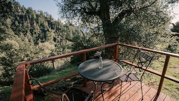 A wooden deck with a metal table and chairs, overlooking a forested area.