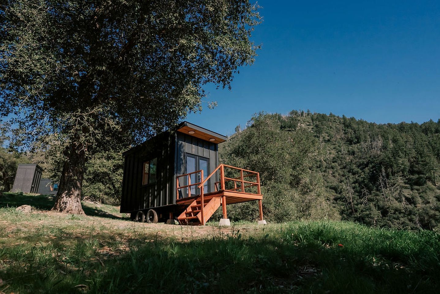 Une petite cabane dotée d’une terrasse en bois et d’un escalier, entourée d’arbres et située au pied d’une colline.